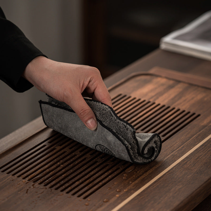 Hand wiping a dark gray tea cloth across a slatted wooden tea tray with the pile side showing