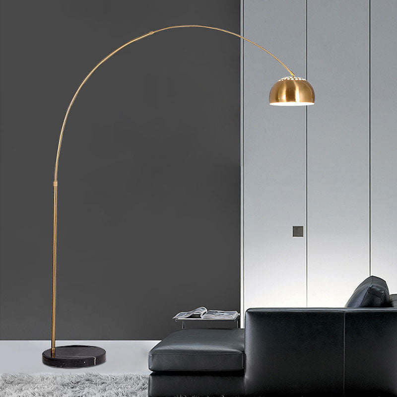 Gold arc floor lamp with a curved arm and round black marble base beside a sofa