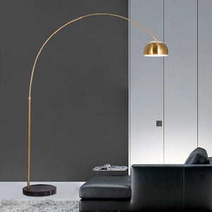 Gold arc floor lamp with a curved arm and round black marble base beside a sofa