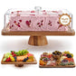 Rectangular acacia cake stand with a clear dome over a pink rose petal cake beside two wooden serving boards, variant view