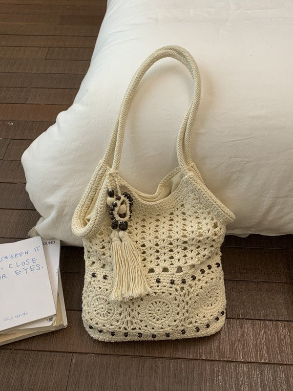 Cream crochet cotton shoulder bag with granny square openwork and a beaded tassel resting on a white pillow