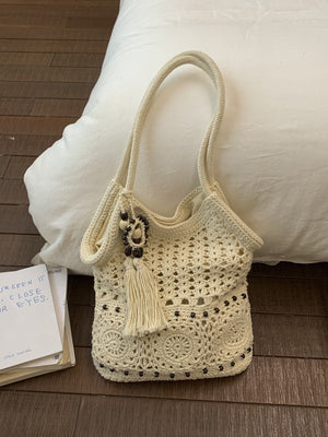 Cream crochet cotton shoulder bag with granny square openwork and a beaded tassel resting on a white pillow