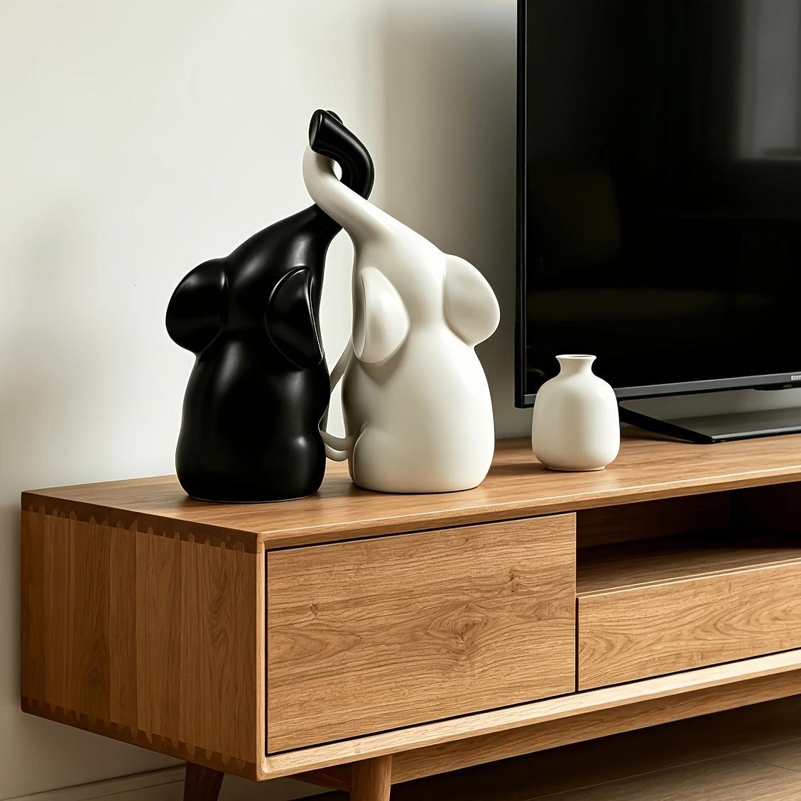 Black and white elephant figurine pair with entwined trunks on a wooden TV console