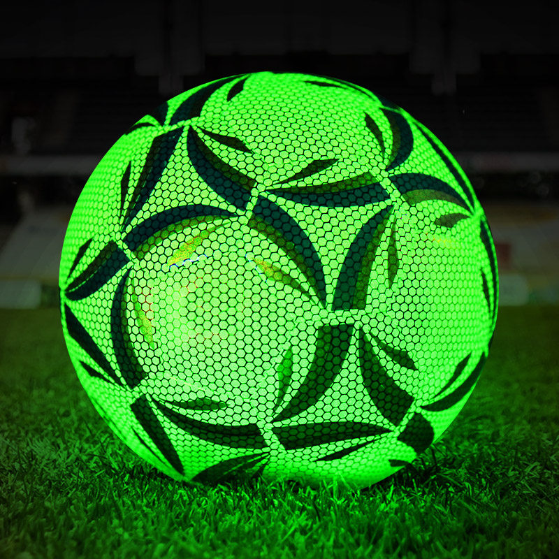Green glowing fluorescent football on grass at night in a stadium, glow in the dark training ball