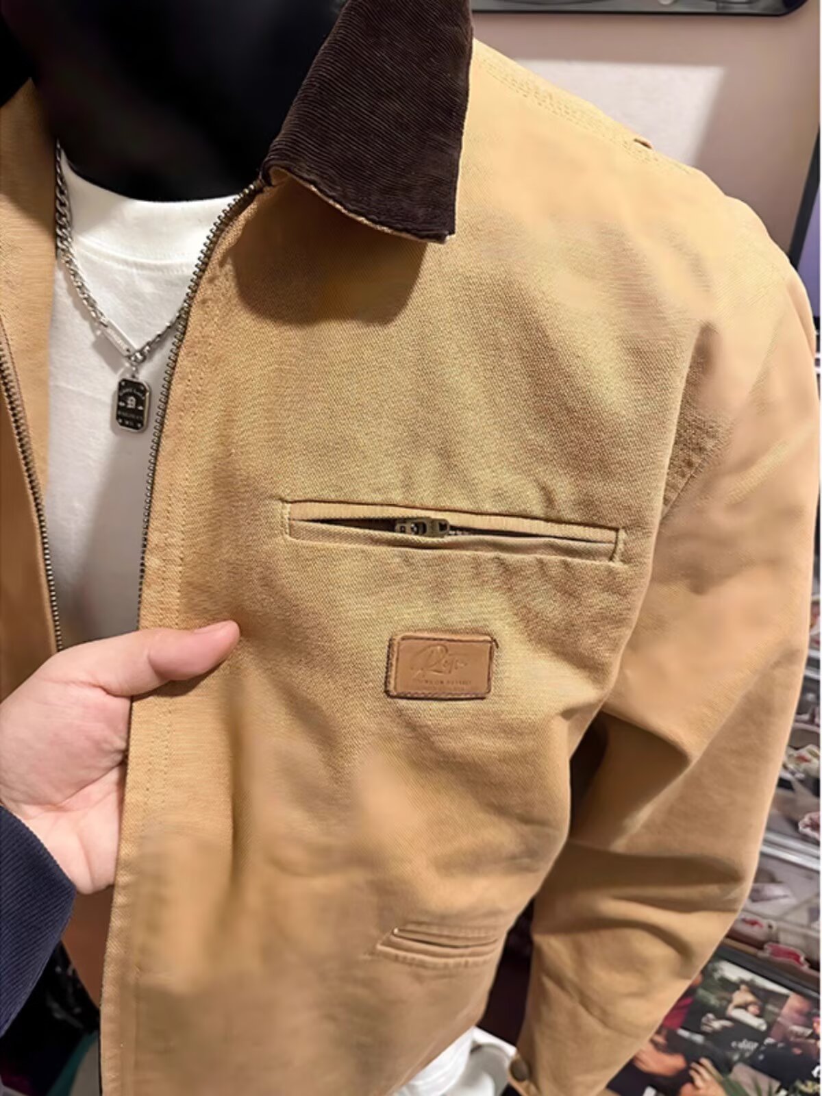 Close view of the khaki jacket chest zip pocket with a small square patch and the dark brown collar