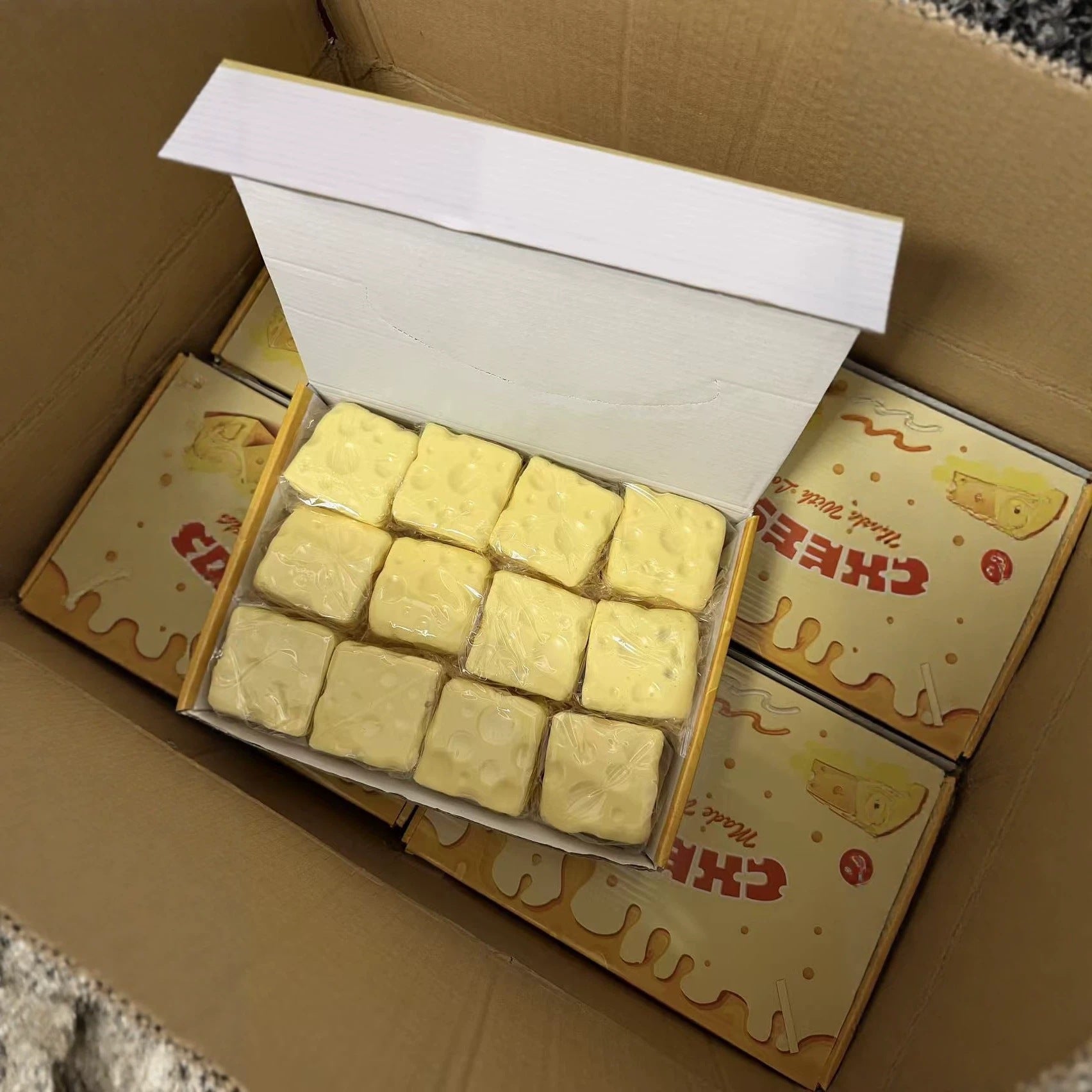 Open counter box holding twelve wrapped pale yellow cheese cube squishies inside a carton