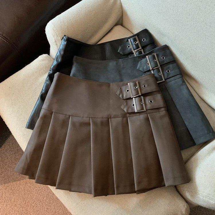 Pleated buckle-strap mini skirts in coffee brown, black and gray on a cream sofa, brown skirt in front