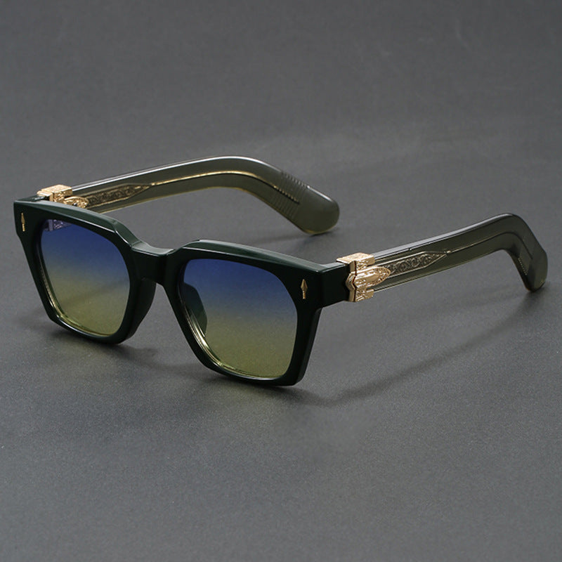 Green square framed sunglasses with wide temples and a gold arrowhead detail on a grey backdrop