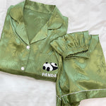 Moss green ice silk pajama set folded on a white bed with a panda chest pocket and elastic waist shorts