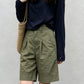 Front view of woman in olive green high-waisted Bermuda shorts with navy tee and woven bag