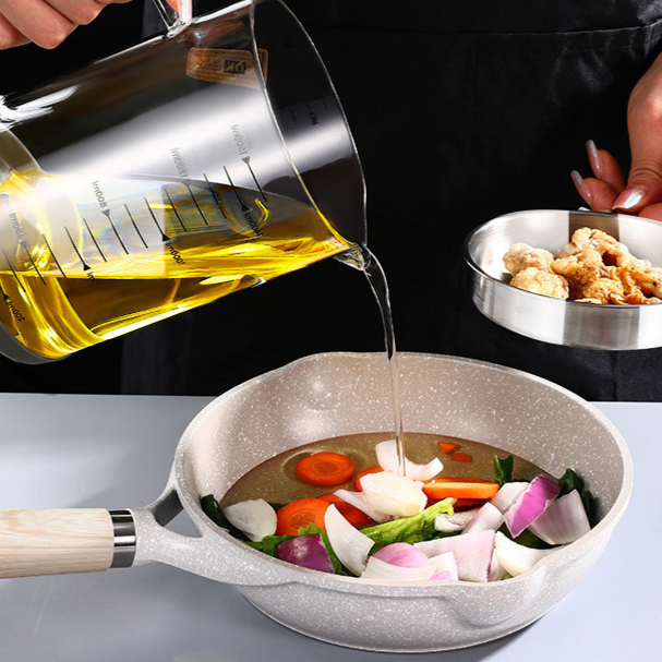 Oil poured from the graduated glass jug into a frying pan of vegetables on a worktop