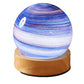 Blue, pink and white striped glass planet night light on a round wooden base, white background