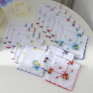 Fanned set of floral cotton handkerchiefs with scalloped colored borders on a light table
