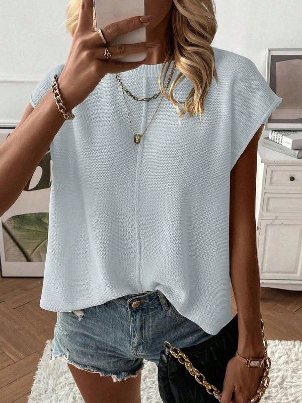 Solid color cap sleeve knit top with a round neck shown on a model against a plain room