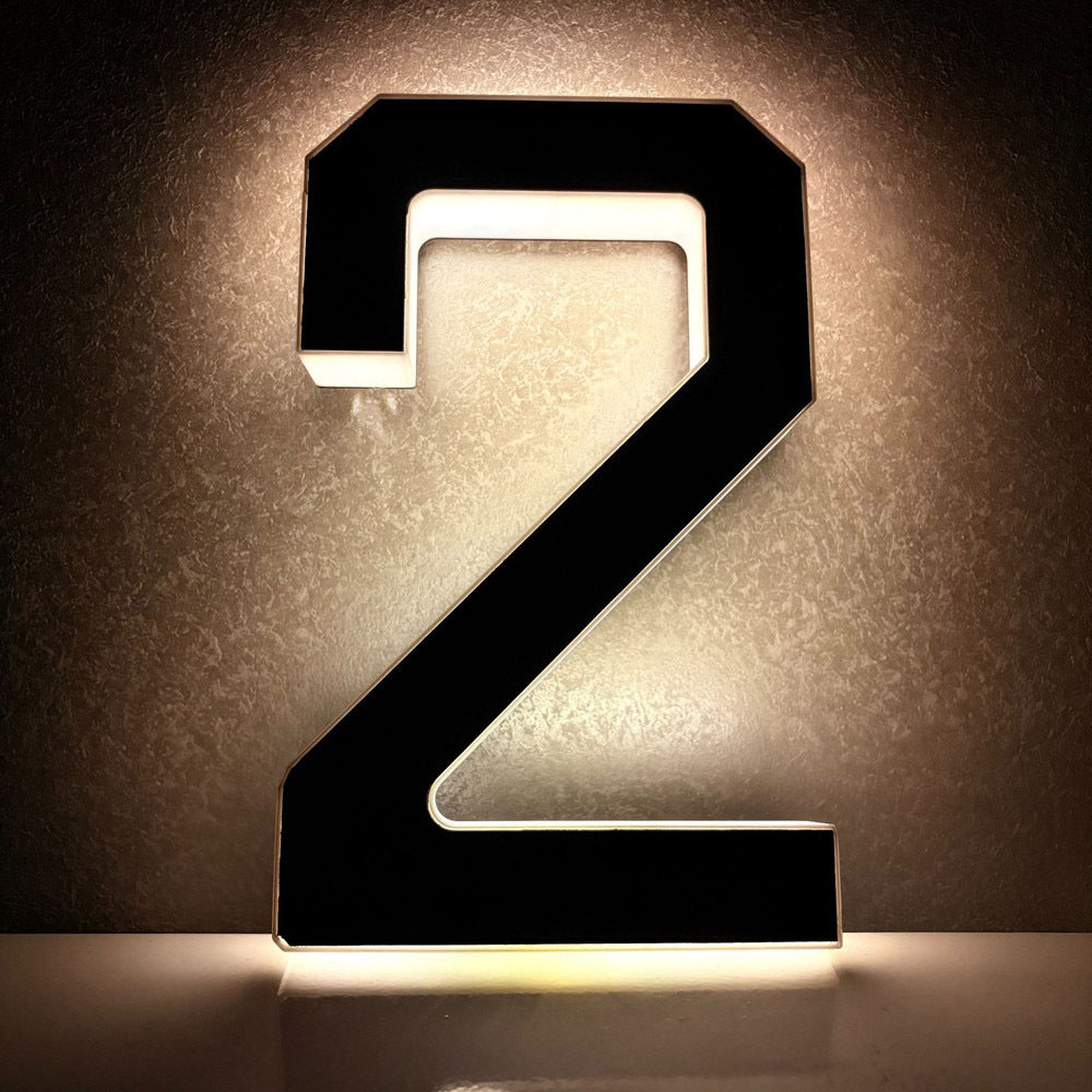 Solar LED house number 2 glowing warm white against a dark textured outdoor wall at night