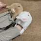One brown and one white bunny plush slipper with pink ears worn with striped trousers on a woven carpet, view 1 of 3