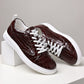 Burgundy embossed lace-up sneakers resting on white blocks, side view with flat white laces and white rubber sole