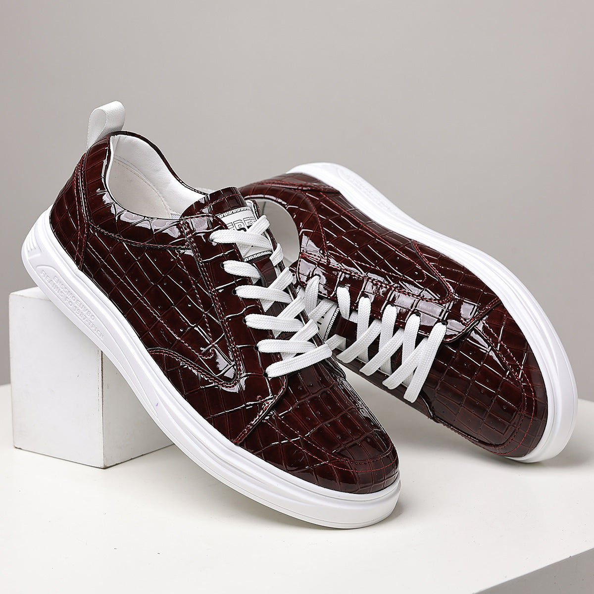 Burgundy embossed lace-up sneakers resting on white blocks, side view with flat white laces and white rubber sole