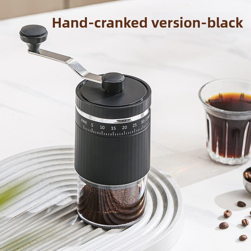 Black hand-cranked coffee grinder with crank arm, fine to coarse scale and clear grounds chamber beside a coffee glass