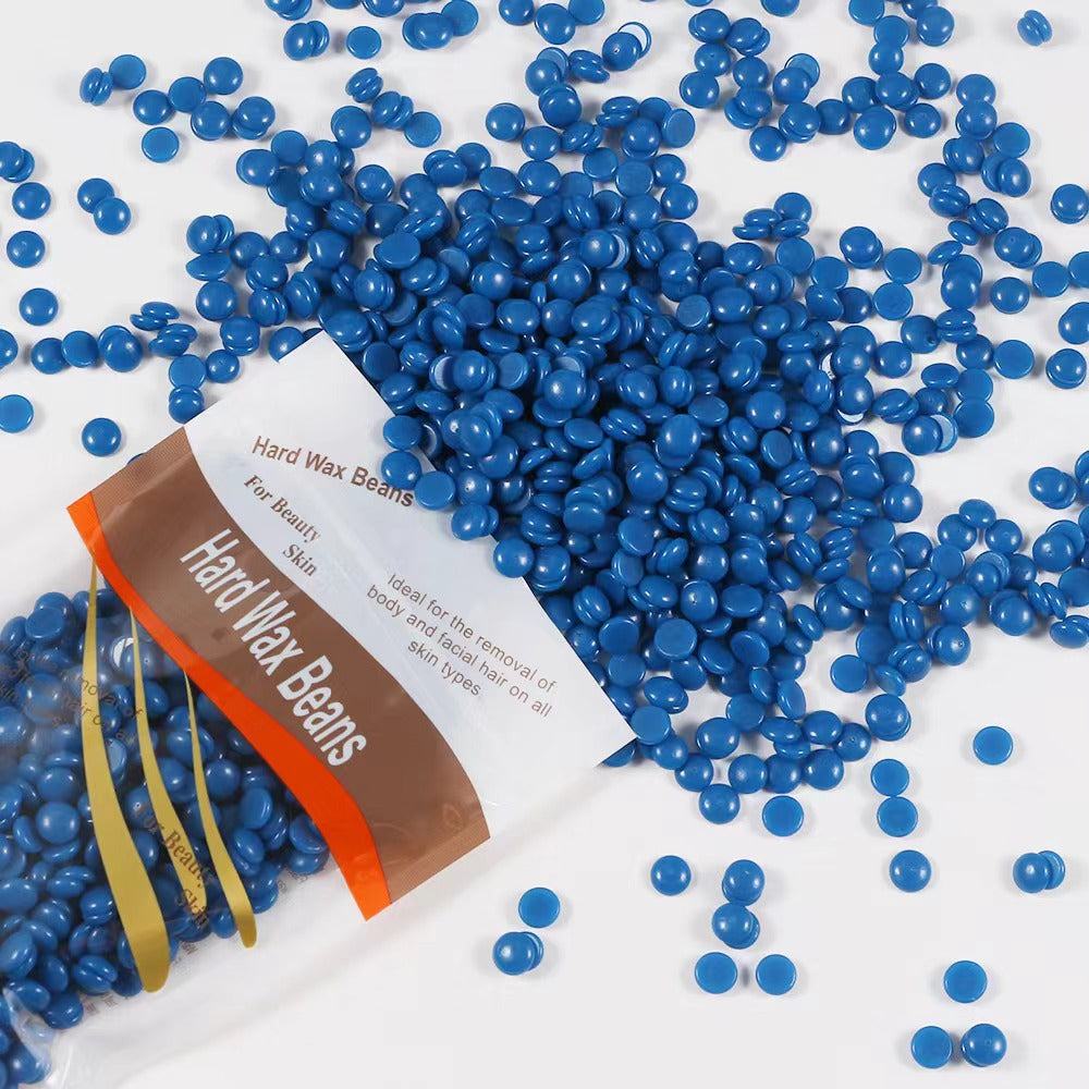Blue hard wax beads spilling from an open pouch across a white surface in a loose drift