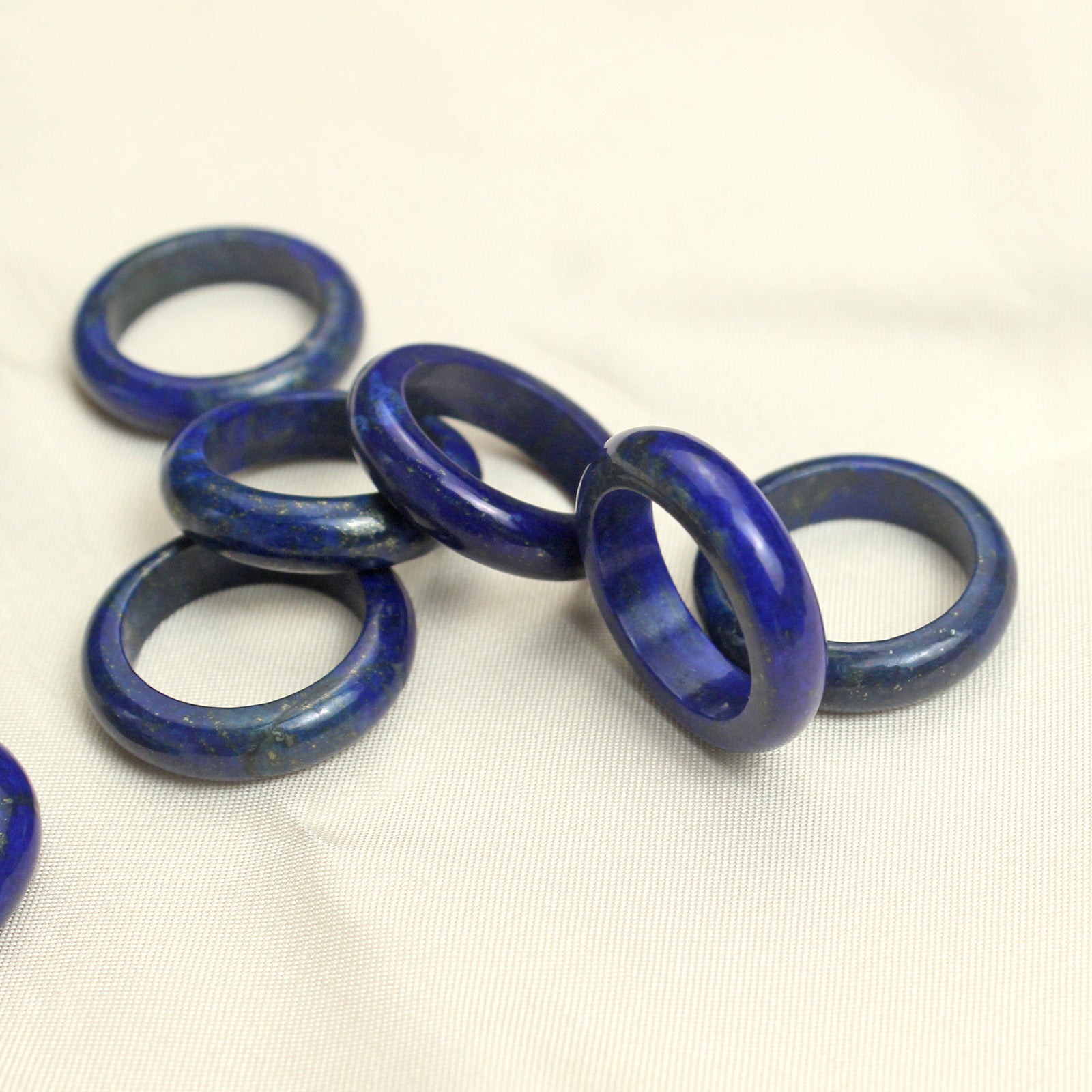 Several lapis lazuli stone band rings grouped on cream cloth, deep blue with scattered gold pyrite
