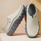 Pair of light gray perforated leather slip-on shoes with gray wavy platform soles on a beige background