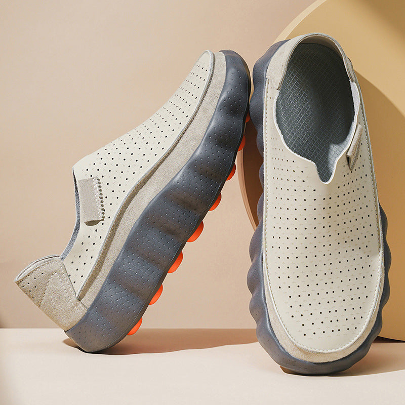 Pair of light gray perforated leather slip-on shoes with gray wavy platform soles on a beige background