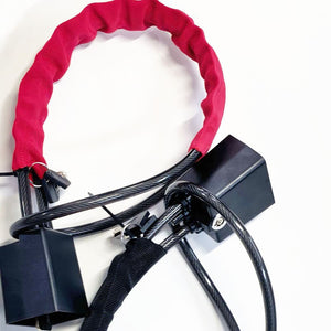 Red sleeve steel cable lock coiled in a loop beside its black lock body and keys
