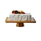 Rectangular acacia wood cake tray on a turned pedestal base holding a white frosted cake with berries and orange slices