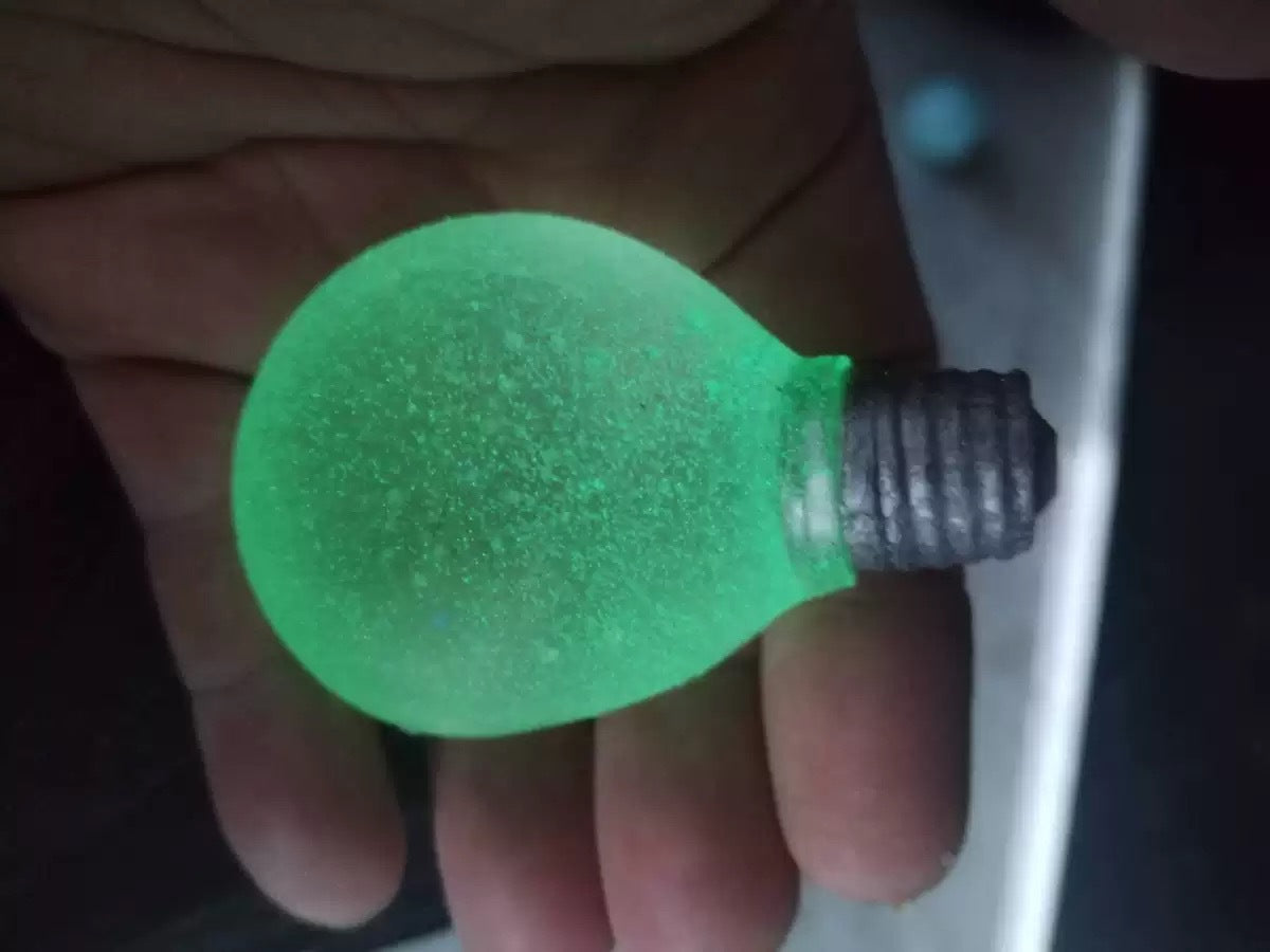 Glow option of the squeeze toy, bulb shape lit flat green in the dark against a hand
