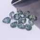 Eleven faceted moss agate pears scattered beside a steel bench blade on white
