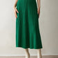 Woman in an emerald green ribbed knit tiered midi skirt with cream ankle boots, hands at her sides