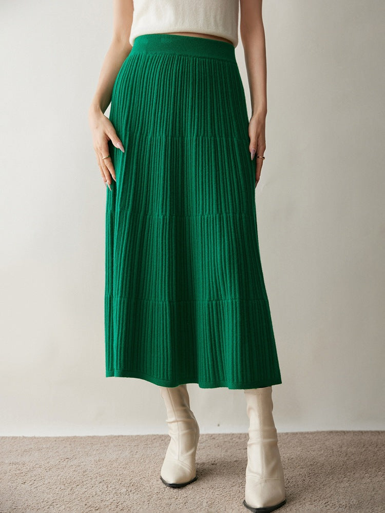 Woman in an emerald green ribbed knit tiered midi skirt with cream ankle boots, hands at her sides
