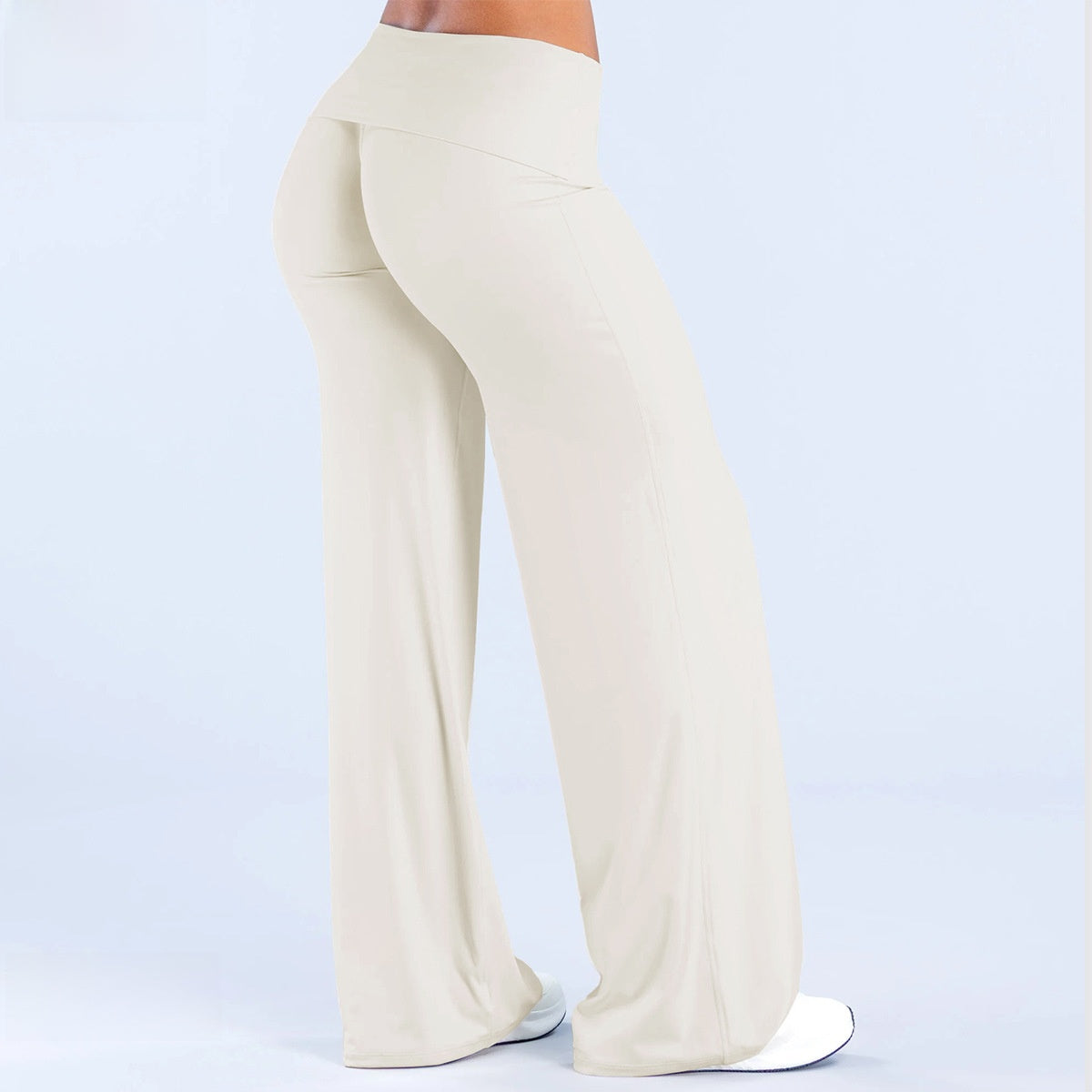 Back view of ivory wide leg pants with a fold over waistband and white sneakers on a pale blue background