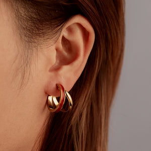 Red enamel gold plated C-shaped hoop earring worn on a models ear from the side