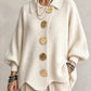 Woman in a cream loose knit top with a shirt collar and five large gold tone buttons, front view