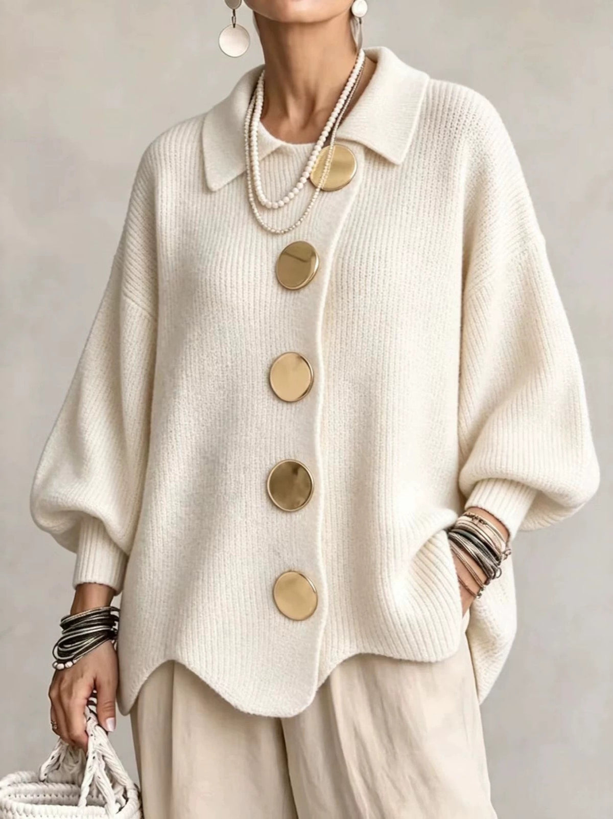 Woman in a cream loose knit top with a shirt collar and five large gold tone buttons, front view