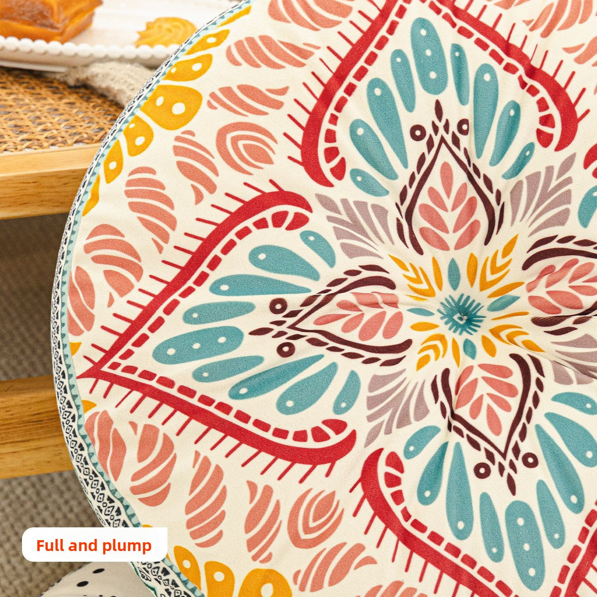 Close up of the coral and teal leaf print top of the round cushion with its pinched center and woven border
