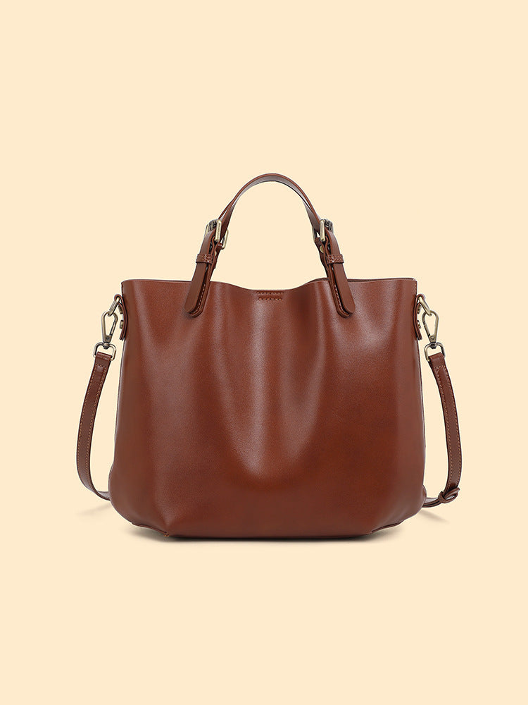 Chestnut brown leather bucket tote with top handles and a detachable shoulder strap on a cream background
