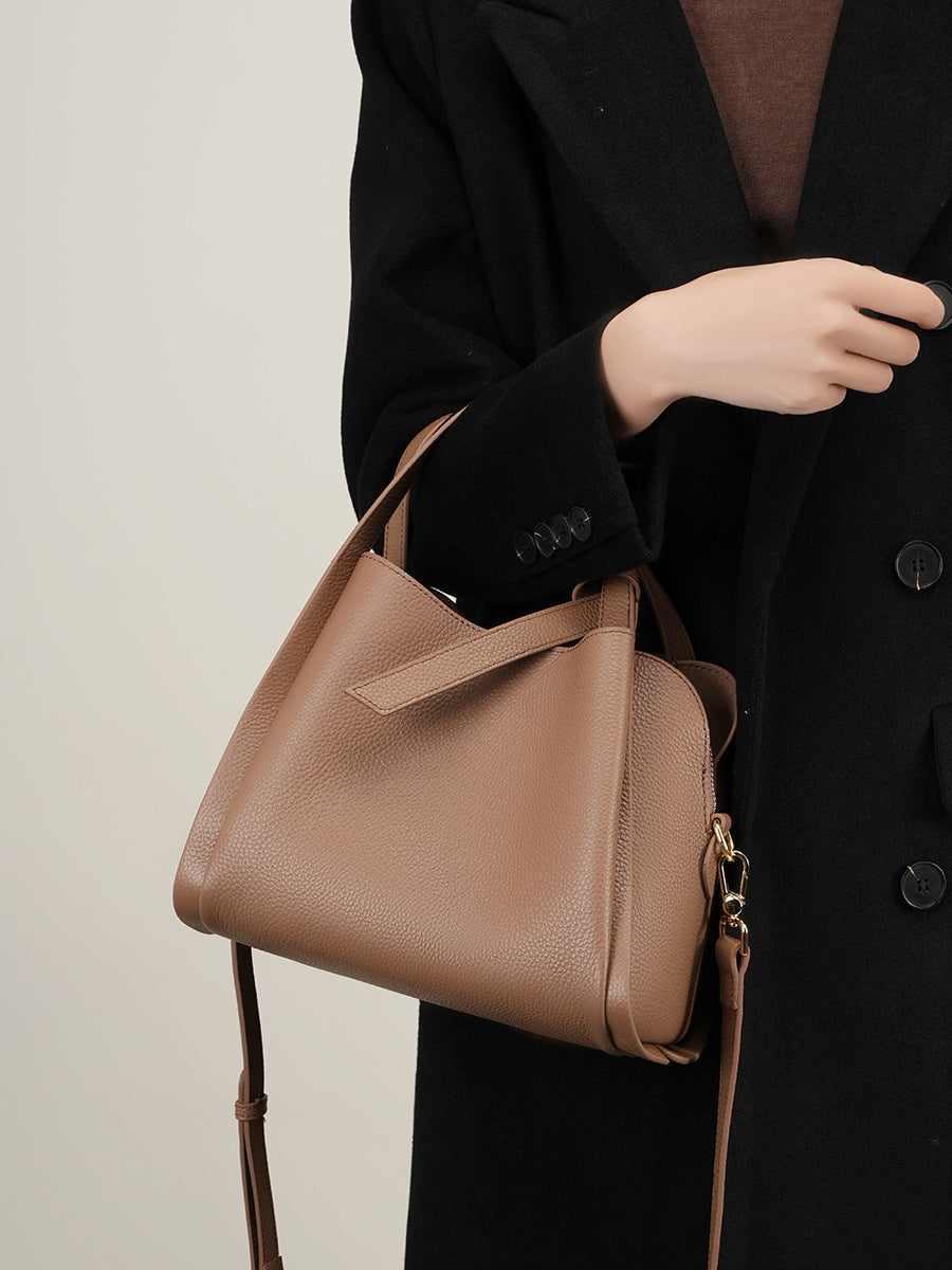 Model holding khaki leather bucket bag by rolled handle with crossbody strap