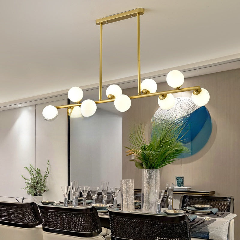 Gold linear pendant light with milky white glass globes above a dining table in a modern room with a green plant