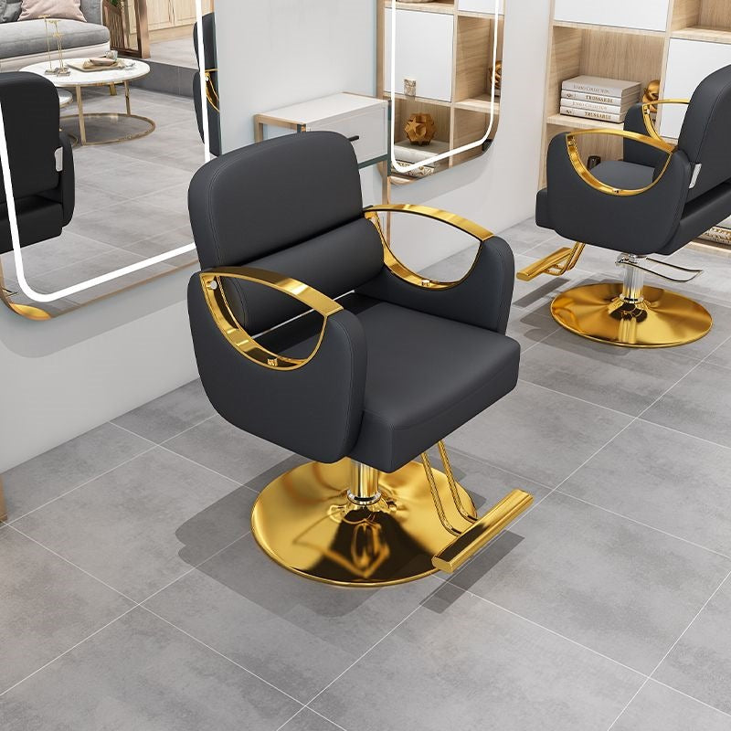 Black salon styling chair with curved gold metal armrests on a gold disc base in a salon