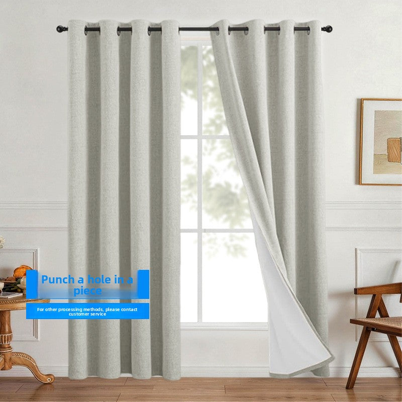 Linen look polyester blackout grommet curtain panel with white thermal backing in even vertical folds beside a window