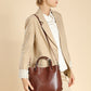 Woman wearing the chestnut brown leather bucket tote crossbody with a beige blazer, side view