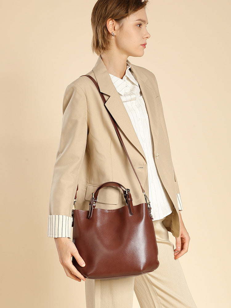 Woman wearing the chestnut brown leather bucket tote crossbody with a beige blazer, side view