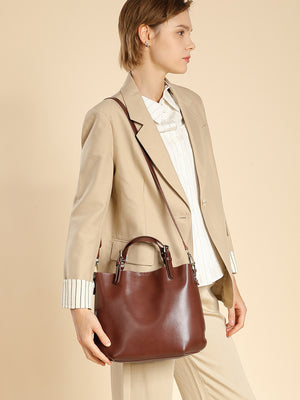 Woman wearing the chestnut brown leather bucket tote crossbody with a beige blazer, side view
