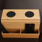 Natural bamboo armrest tray with two round black pads and a side compartment holding a remote and a phone