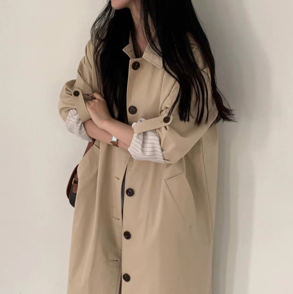 Light khaki long single breasted trench coat with lapel collar and buttoned front on a model