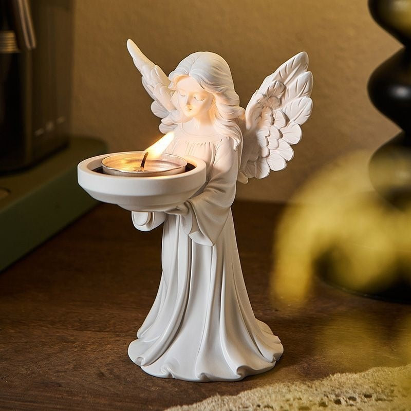White matte angel figure holding a dish with a tea light, front view on a wood table