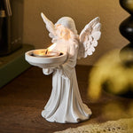 White matte angel figure holding a dish with a tea light, front view on a wood table